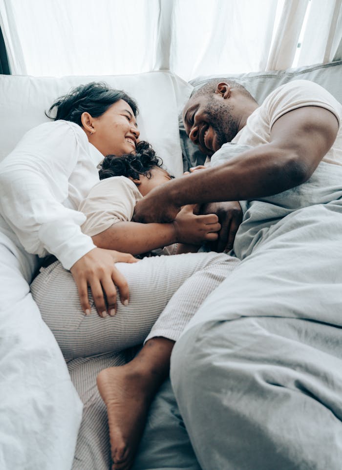 A family enjoys a loving and relaxing morning embrace in bed, expressing warmth and happiness.