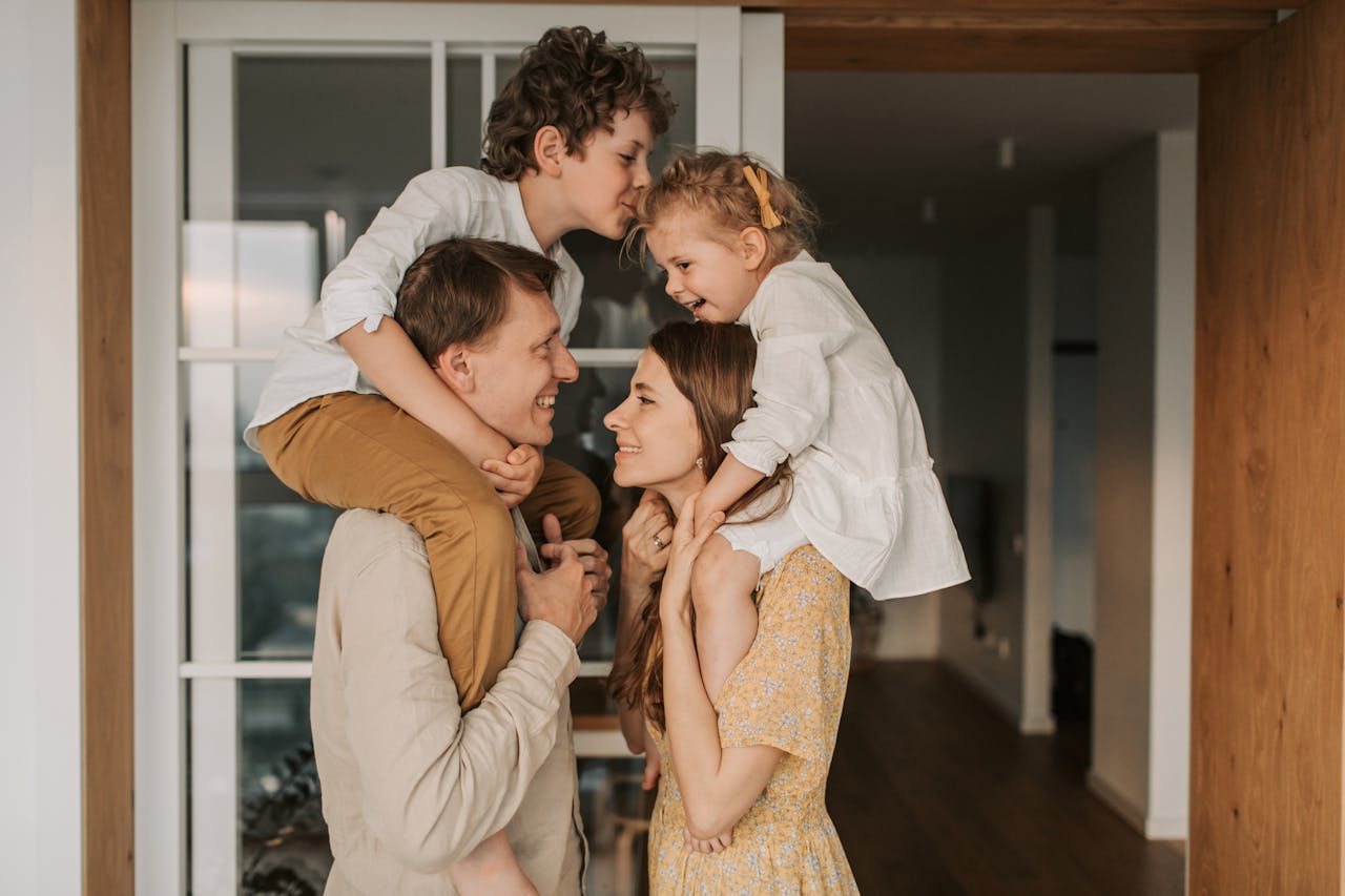 Family enjoying a playful moment indoors with children on parents' shoulders.