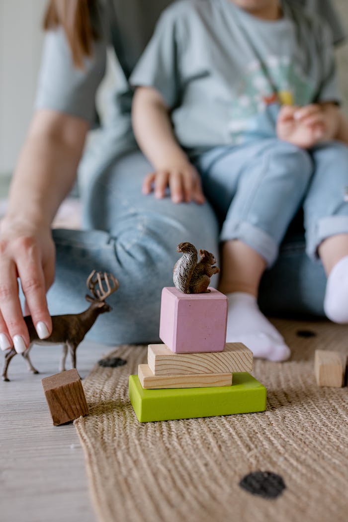 A mother and child play together with wooden blocks and toy animals on a textured rug indoors.